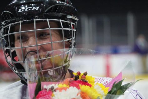 A girl with a hockey helmet on holds a bouquet of flowers while smiling