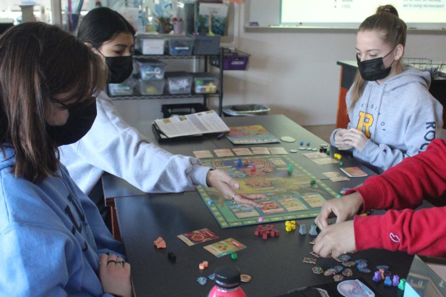 four students sit at a table playing a board game about cells and cancer