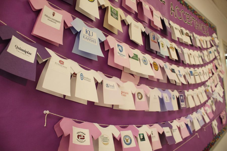 Paper shirts with the names of colleges that seniors at Holy Cross have gotten accepted too are hung up on a bulletin board.